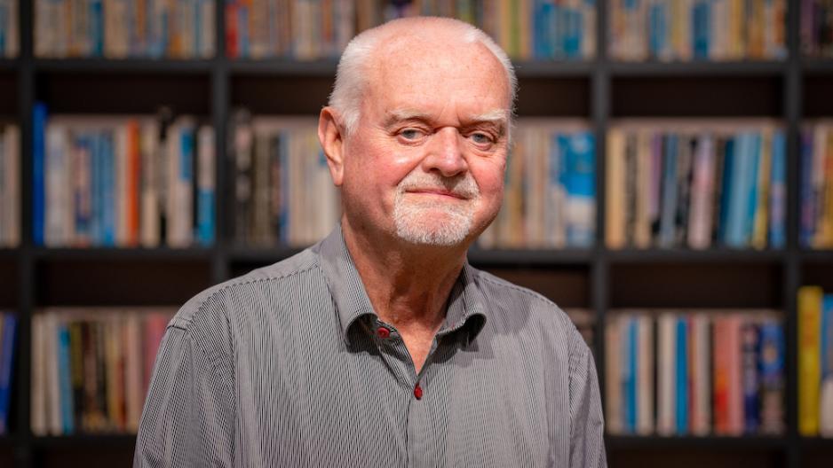 Rune Ottosen st&aring;r foran en bokhylle og ser i kameraet. 