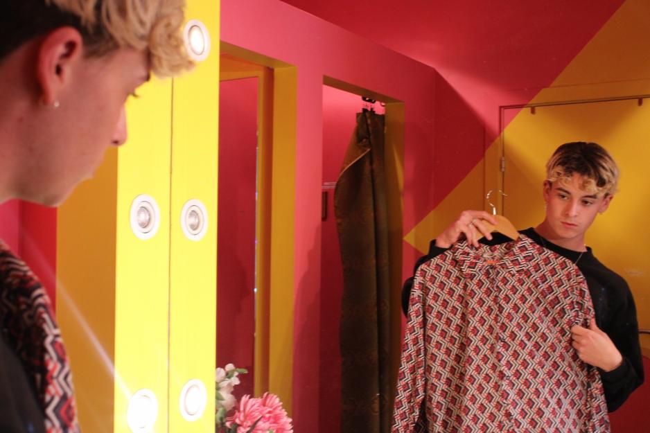 Phillip Eskildsen ser seg i speilet og holder en r&oslash;d m&oslash;nstret skjorte opp foran seg. 