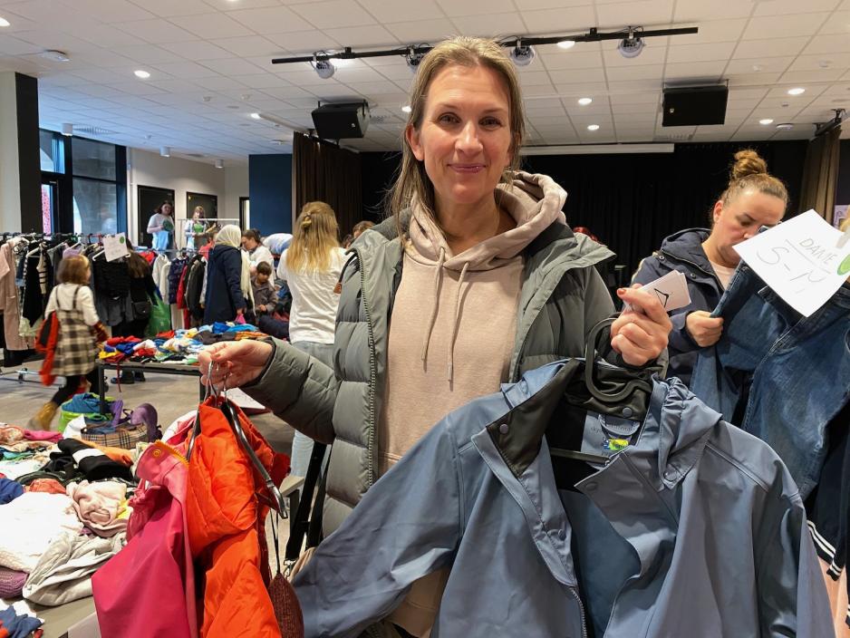 dame som st&aring;r med flere klesplagg, blant annet regnjakker til barn