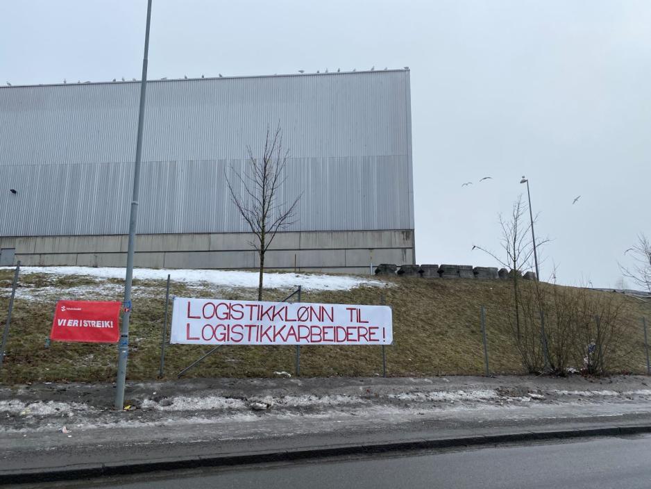 Skilt p&aring; andre siden av en vei som sier "logistikkl&oslash;nn til logistikkk arbeidere"