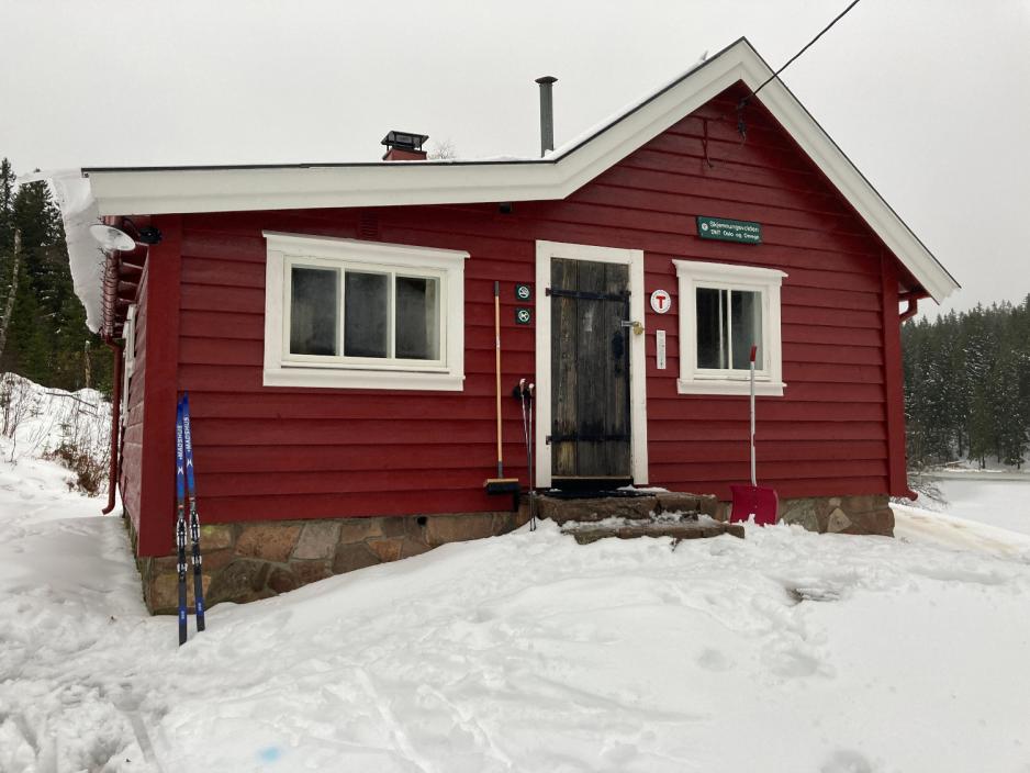 Den r&oslash;de hytten Skjennungsvolden i sn&oslash;rike omgivelser. Den har to vinduer ved inngangsd&oslash;ren, med hvite vinduskarmer. Det st&aring;r ski ved hytteveggen. 