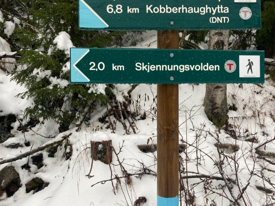 Et skilt som blant annet peker mot Skjennungsvolden og som sier at det er to kilometer dit. Det er sn&oslash; i bakgrunnen. 