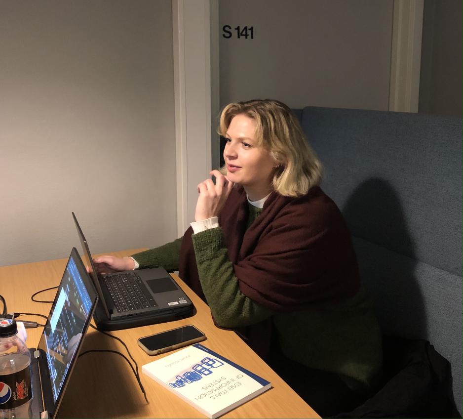 En jente sitter ved et bord og ser opp p&aring; venninnen sin.