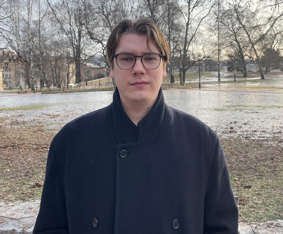 Mann i i slutten av 20-&aring;rene st&aring;r rett opp og ned og ser i kamera i Slottsparken. Han har p&aring; seg bl&aring; parkas