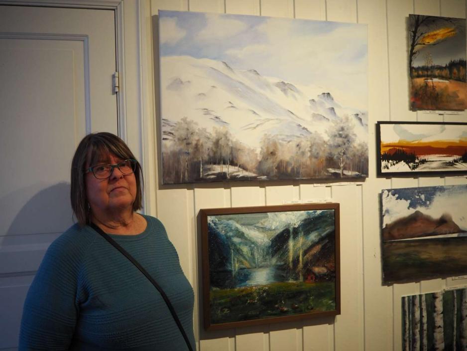 Ulla Kristoffersen st&aring;r ved eget maleri av fjell i Valdres