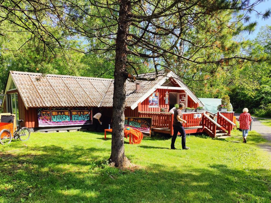 r&oslash;d hus i solen med to mennesker utenfor 