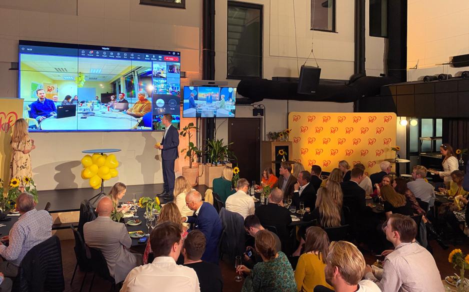 Oversiktsbilde over rommet der KrFs valgvake holdes, med flere mennesker og valgkampen p&aring; storskjerm