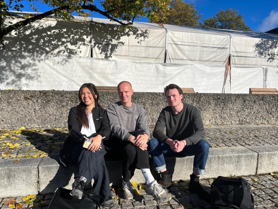 Tre studenter sitter ute p&aring; p&aring; en steintrapp