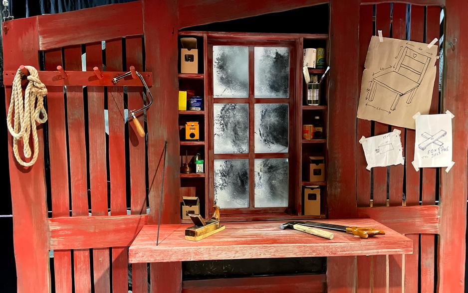 Bildet viser et n&aelig;rbilde av Snekker Andersens verksted. Bruksanvisninger, en hammer og en sag er blant utstyret som ligger p&aring; den r&oslash;de arbeidsbenken. 