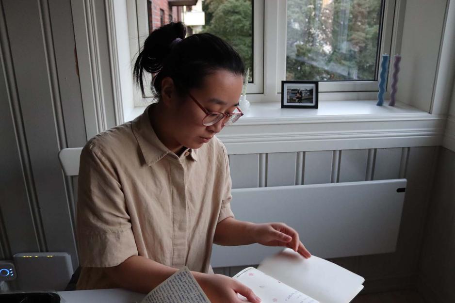 Xueqi Pang sitter p&aring; en trestol og leser gjennom sine gamle dagb&oslash;ker.