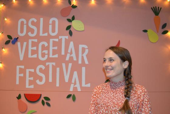 Ung kvinne st&aring;r foran Oslo Vegetarfestival-skilt og smiler