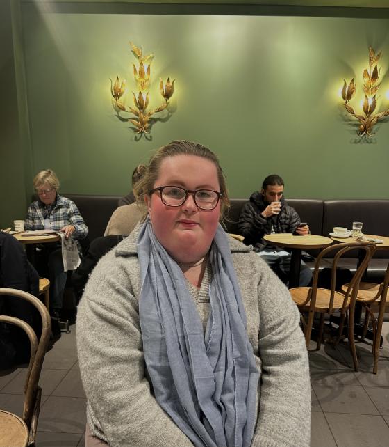 en jente sitter i et kafelokale med bl&aring;tt skjerf