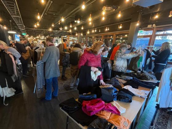 Klesbyttemarked p&aring; Biblioteket. Stativer med kl&aelig;r og ivrige deltakere