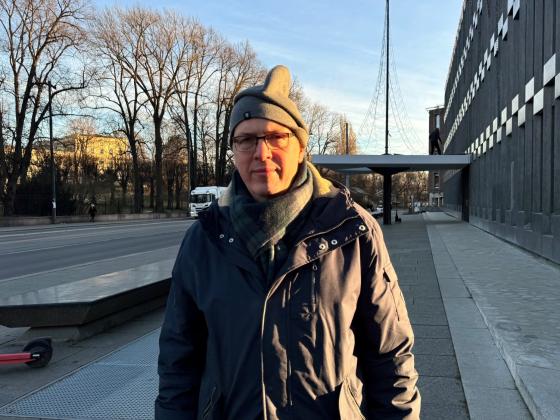 Ola Manns&aring;ker utenfor den gamle amerikanske ambassaden med sidelys fra morgensolen. Har p&aring; ytterkl&aelig;r: lue, skjerf og tykk jakke. Seri&oslash;st ansiktsuttrykk. 