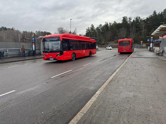Det er to r&oslash;de ruter-busser p&aring; holdeplassen.