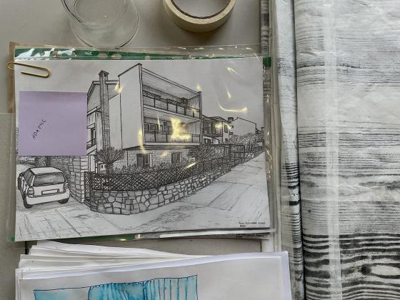 P&aring; en pult ligger det en skisse av et hus. Foran huset er det er gjerde og en bil "parkert" utenfor.