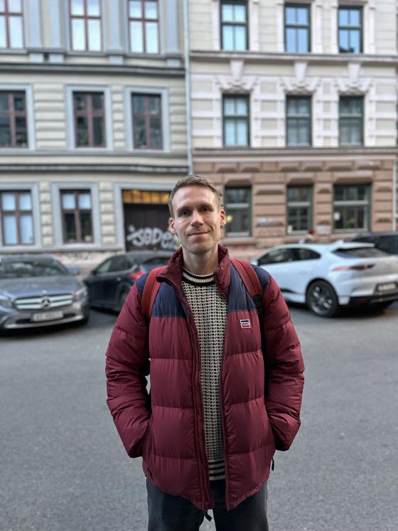 Mann st&aring;r i gata og smiler til kamera. Han har p&aring; islender og r&oslash;d boblejakke. 