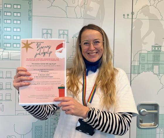 Hege Fr&oslash;ystad holder opp plakaten til "Barnas Julehjelp" mens hun smiler til kameraet