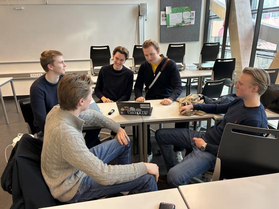 Unge gutter sitter ved en pult og snakker om ungdomsbedriften sin