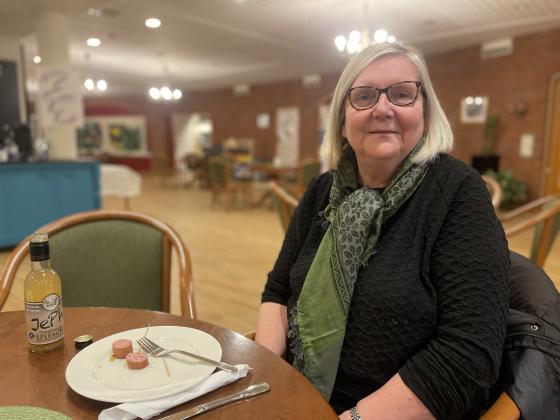 Solveig sitter ved et bord og spiser p&oslash;lse og drikker eplemost. 