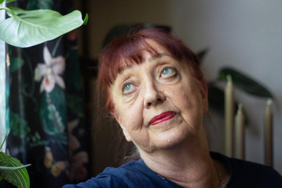 Portrett av en eldre dame med r&oslash;dt oppsatt h&aring;r og pannelugg. Hun har blikket rettet mot et vindu. I bakgrunnen ser man en plante, noen lys og gardiner