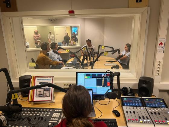 Programleder styrer livesending p&aring; radio og ser inn p&aring; studio. 