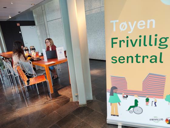 T&oslash;yen Frivillighetssentral som plakat. Sitter to stk ved et oransje bord og prater.