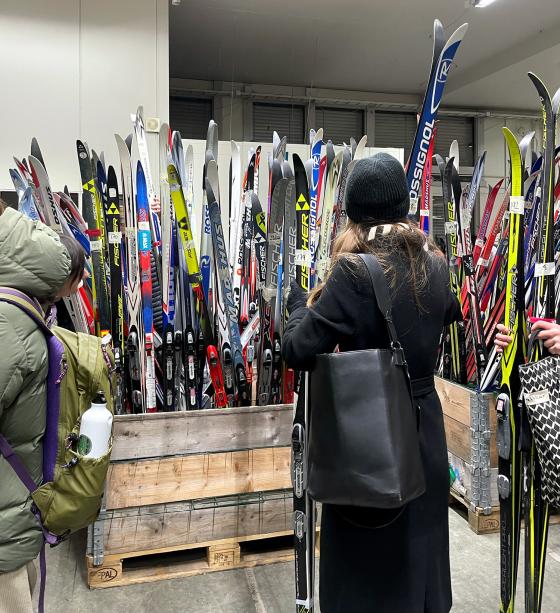 Mange langrennski st&aring; rett opp og ned i en kasse. En kvinne st&aring;r forran kassen og holder et parr med langrennsski