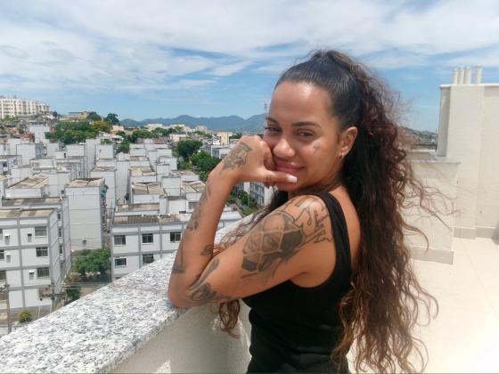 En kvinne st&aring;r p&aring; en takterrasse og smiler mot kamera