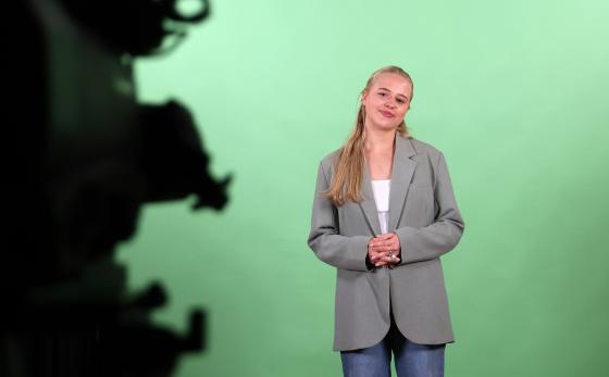 Blond dame st&aring;r forran en gr&oslash;nn vekk et uskarpt kamera er til h&oslash;yre i bildet
