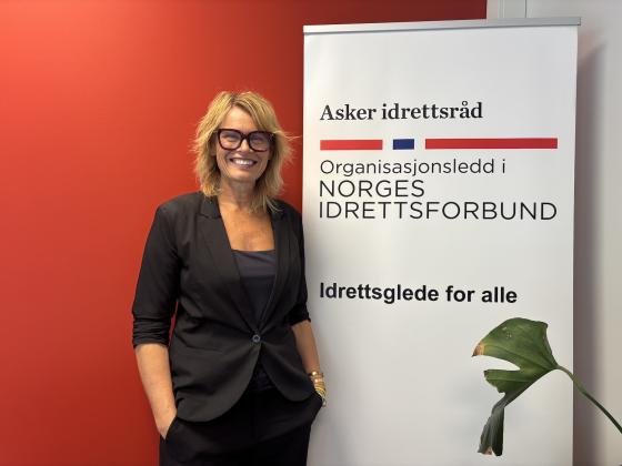 Gry Elisabeth Garlie, daglig leder i Asker idrettsråd, ved siden av en plakat