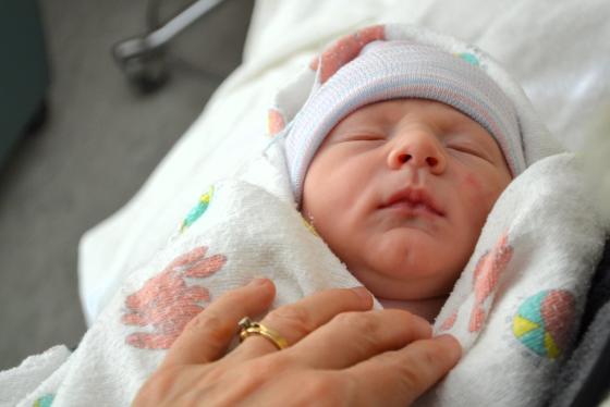 Lite nyf&oslash;dt barn pakket inn i laken i fanget til mamma 