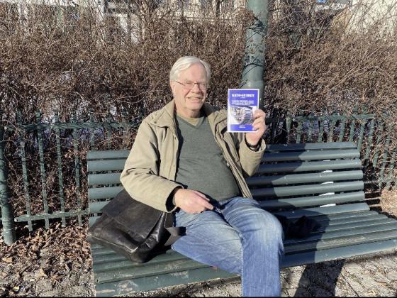 Geir Hem sitter p&aring; en benk med en brosjyre i h&aring;nda.