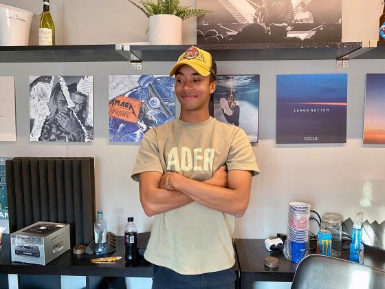 Artist Adrian Amara st&aring;r foran en vegg i studioet sitt med bilder av tidligere album han har laget. 