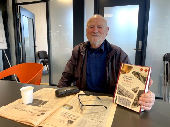 mann holder opp boka han har l&aring;nt mens han drikker kaffe og leser dagens avis