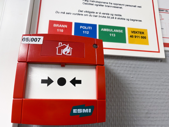 Bilde av en r&oslash;d brannvarsler med n&oslash;dnummerene bak. Bildet er tatt p&aring; OsloMet