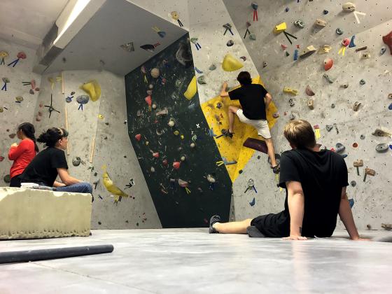 En person klatrer i en klatrevegg mens andre ser p&aring;