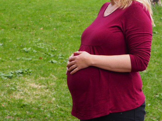 Gravid dame i r&oslash;d genser tar seg p&aring; magen. 
