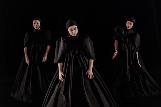 Tre dansere p&aring; en m&oslash;rk scene og sorte kostymer. 