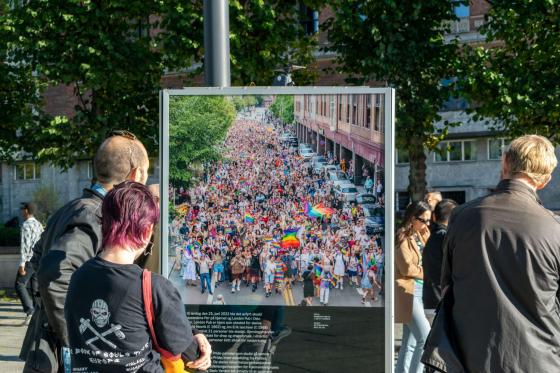 Folk st&aring;r og ser p&aring; et bilde av pride parade