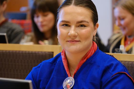 Portrettbilde av Elle i kofte, med en pin p&aring; den. Hun sitter i rettssal, i en pause f&oslash;r Fosen-rettsaken fortsetter. I bakgrunnen er andre koftekledde. 