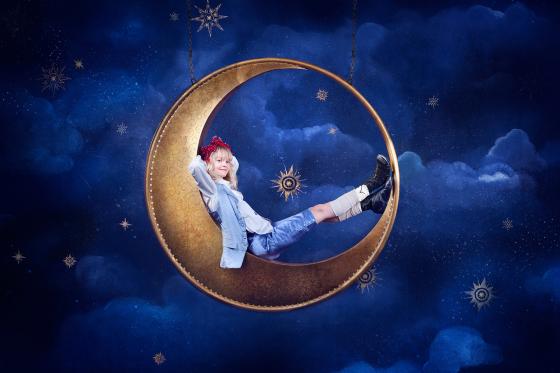 Monica Dybwad sitter i en halvm&aring;nerekvisitt med en bl&aring; bakgrunn.