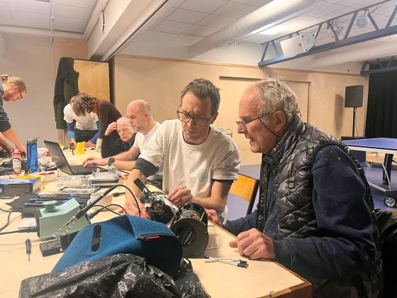 En eldre mann og en litt yngre mann sitter ved et bord og pr&oslash;ver &aring; fikse noe. 