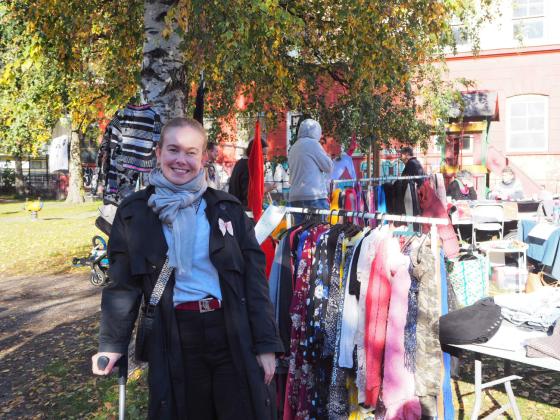 Dame st&aring;r foran et stativ med kl&aelig;r p&aring; et loppemarked