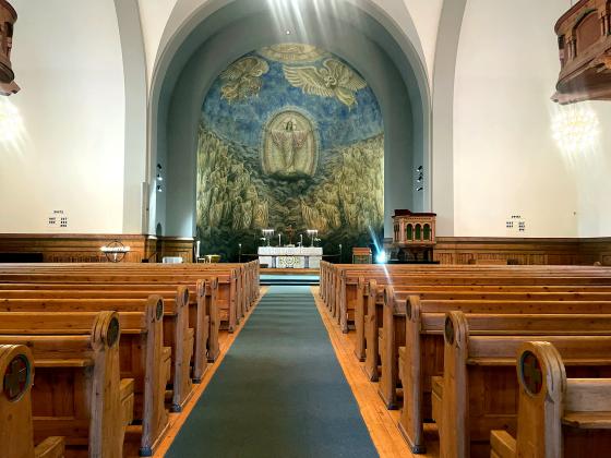 Innsiden av en kirke hvor man ser benkene p&aring; hver sin siden. i Midten av bildet ser man alteret