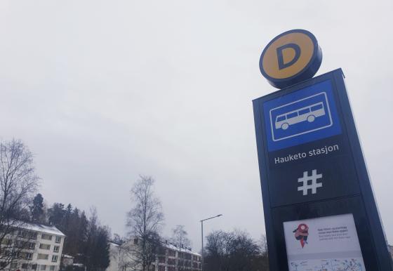 Gr&aring; himmel over et skilt for Hauketo bussholdeplass