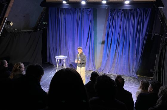 Komiker p&aring; scenen foran bl&aring; bakgrunn