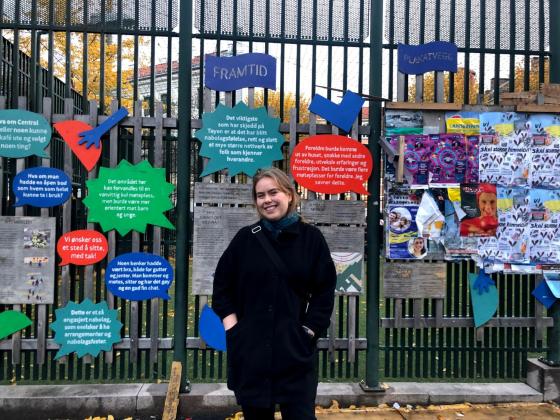 kvinne st&aring;r ute, foran vegg med fargerike snakkebobler