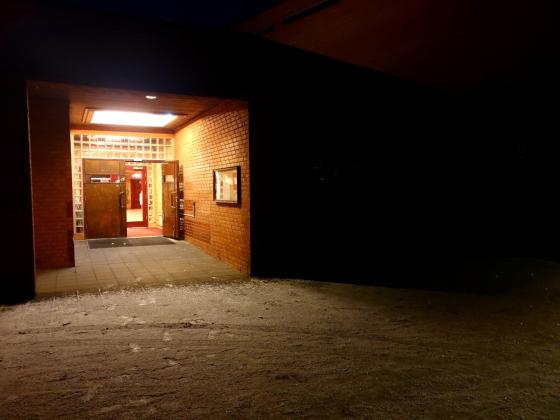 Inngangsparti til en kirke i murstein, d&oslash;ren er &aring;pen og det er lyst inne, mens det er helt m&oslash;rkt utenfor