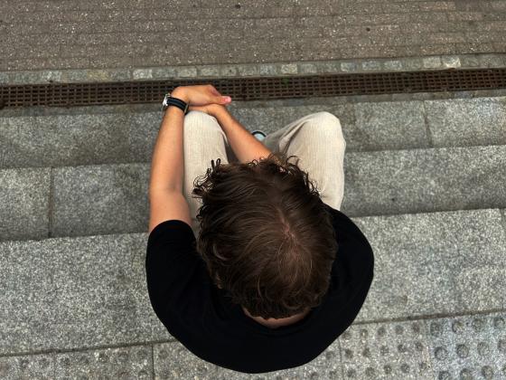 Gutt som sitter p&aring; trappen med hodet vendt ned, bildet er tatt ovenfra